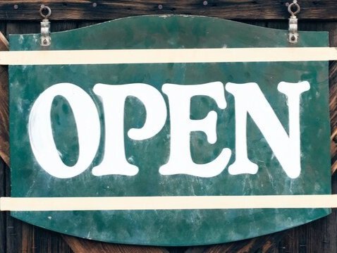 Green "OPEN" sign hanging on a wooden background, indicating that a business is open for customers.